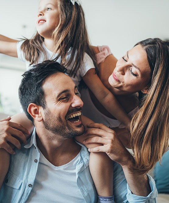 A father laughing while giving his young daughter a piggyback ride